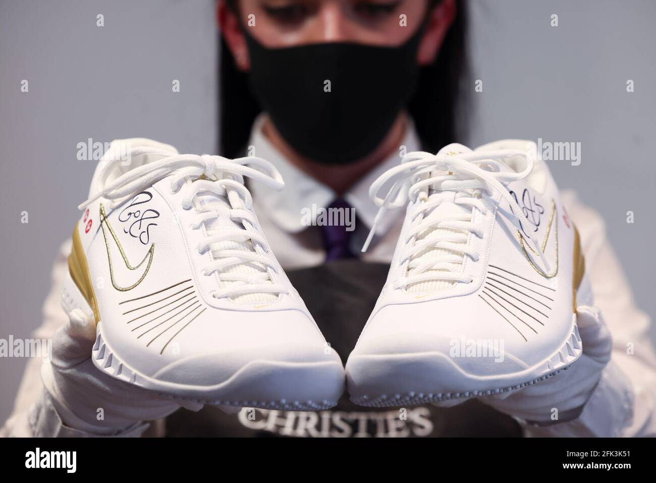 Un asistente de la galería de Christie posará con zapatillas de deporte del  lote 'The Championships, Wimbledon, 2007' incluido en 'The Roger Federer  Collection', que se venderá en subasta, en la casa