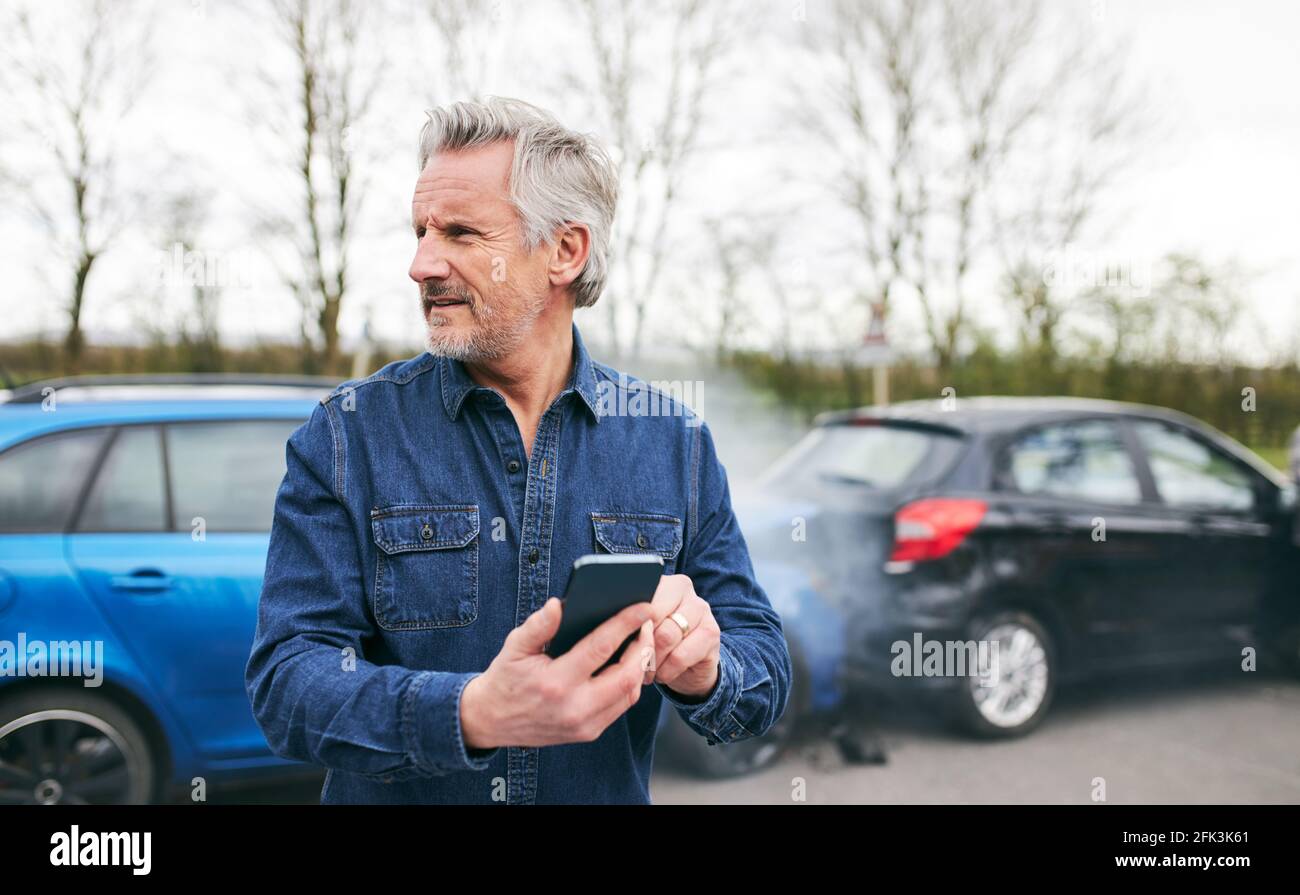 Un hombre mayor de pie cerca de un coche dañado después de llamar por accidente de tráfico empresa de recuperación de averías utilizando el teléfono móvil Foto de stock