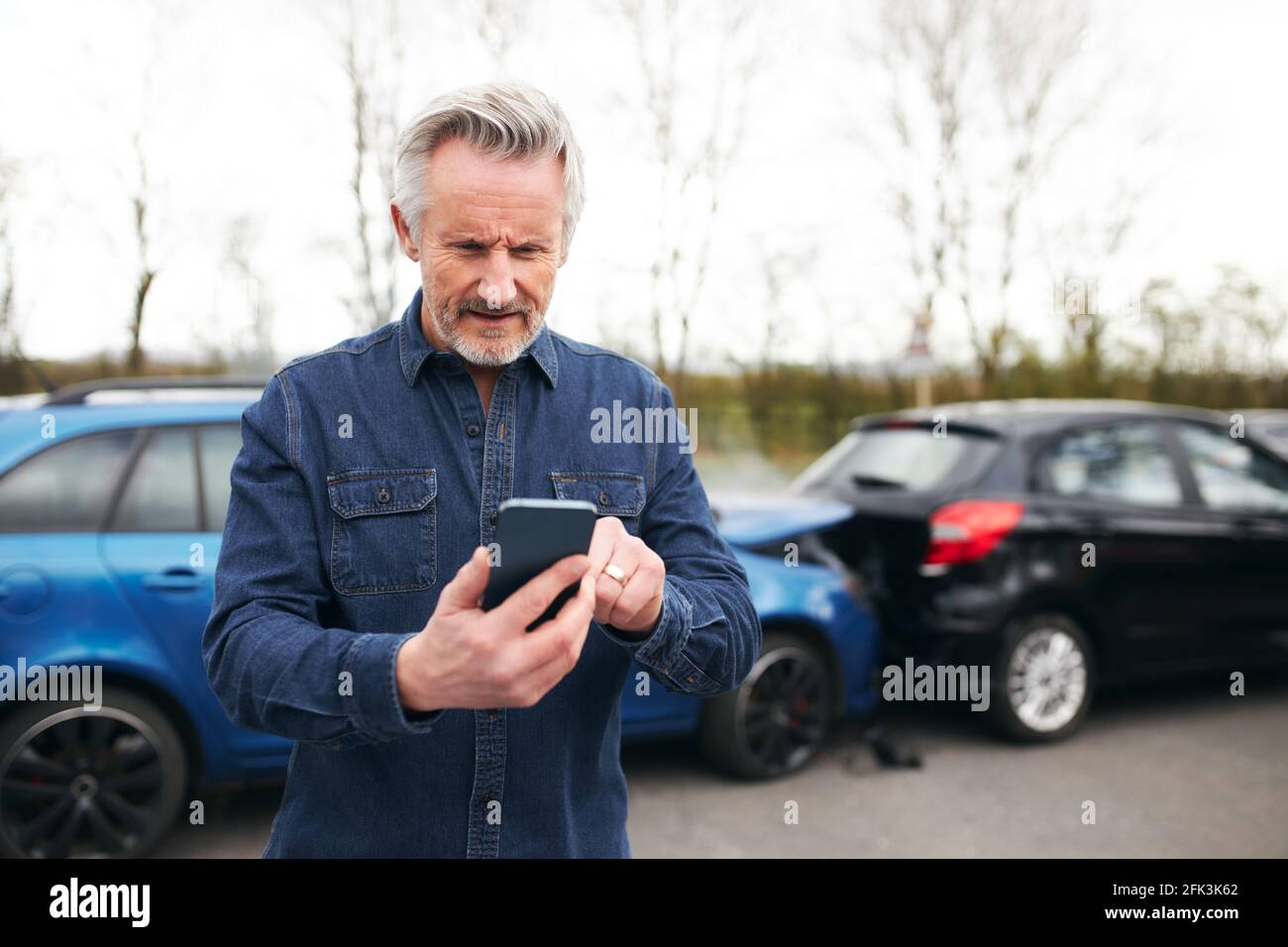 Un hombre mayor de pie cerca de un coche dañado después de llamar por accidente de tráfico empresa de recuperación de averías utilizando el teléfono móvil Foto de stock