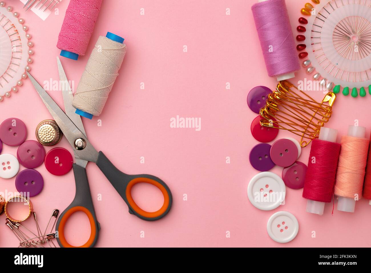 Accesorios de costura incluyendo bobinas de hilo y pins sobre fondo rosa Foto de stock