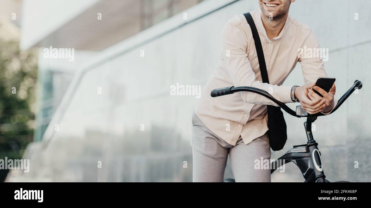 Hombre Adulto Caminando A La Oficina Con Una Mano Sosteniendo La Bicicleta  Y La Otra Mano Mirando Su Teléfono Móvil. Concepto De Transporte Ecológico  Fotos, retratos, imágenes y fotografía de archivo libres