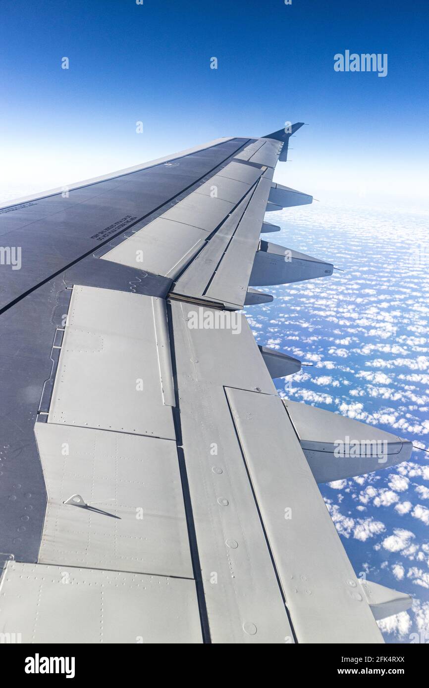 La vista desde la ventana del ala de un avión de reacción mirando hacia abajo sobre un cielo azul con suaves nubes blancas Foto de stock