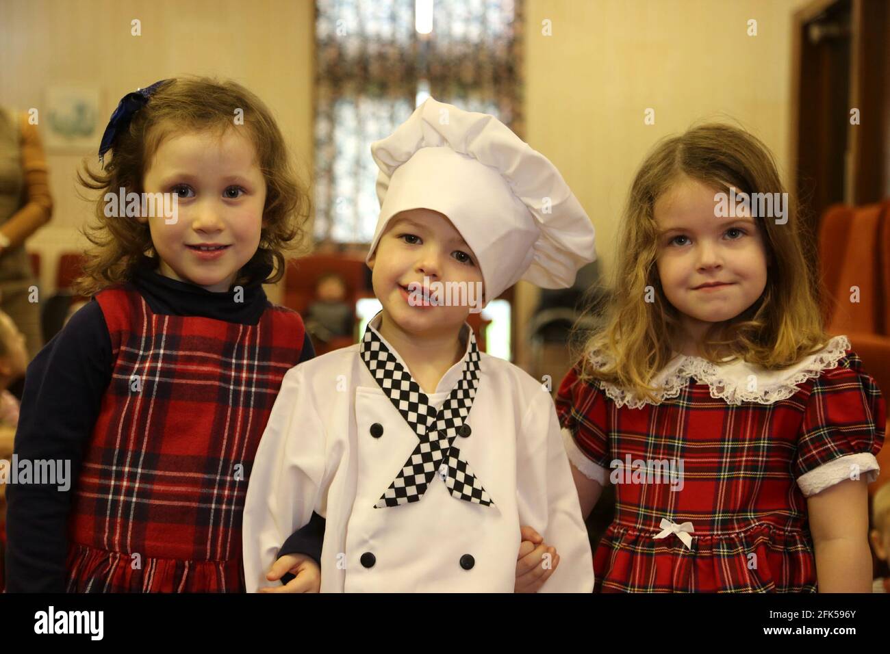 Escuela Primaria Tarbolton, Ayrshire, Escocia, Reino Unido. 26 Jan 2016 Cena  de Burns para niños de la guardería y de la Primaria. Niño vestido como  chef flanqueado por dos niñas con trajes