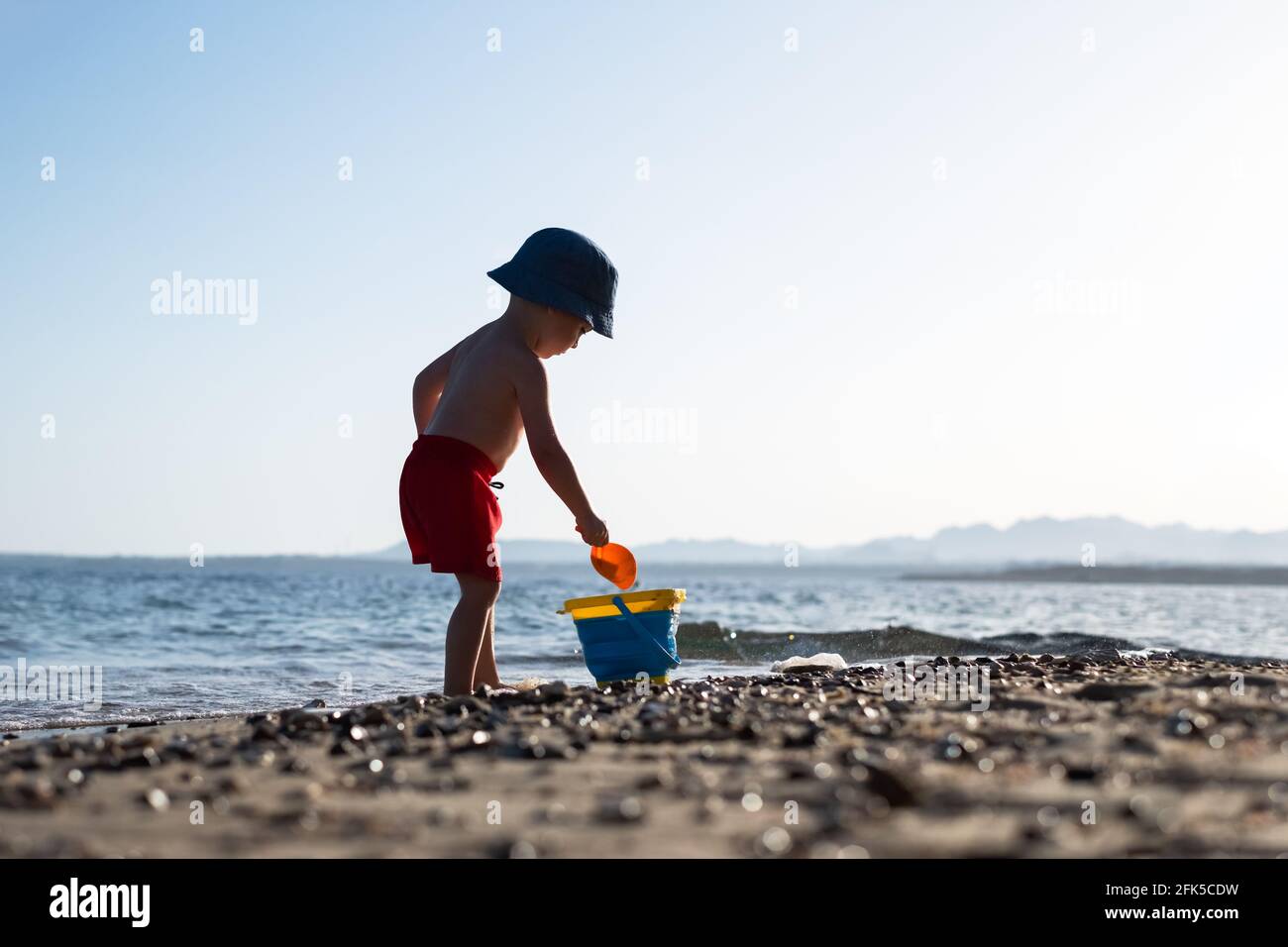 Niño en pantalones cortos rojos en la playa de verano Foto de stock