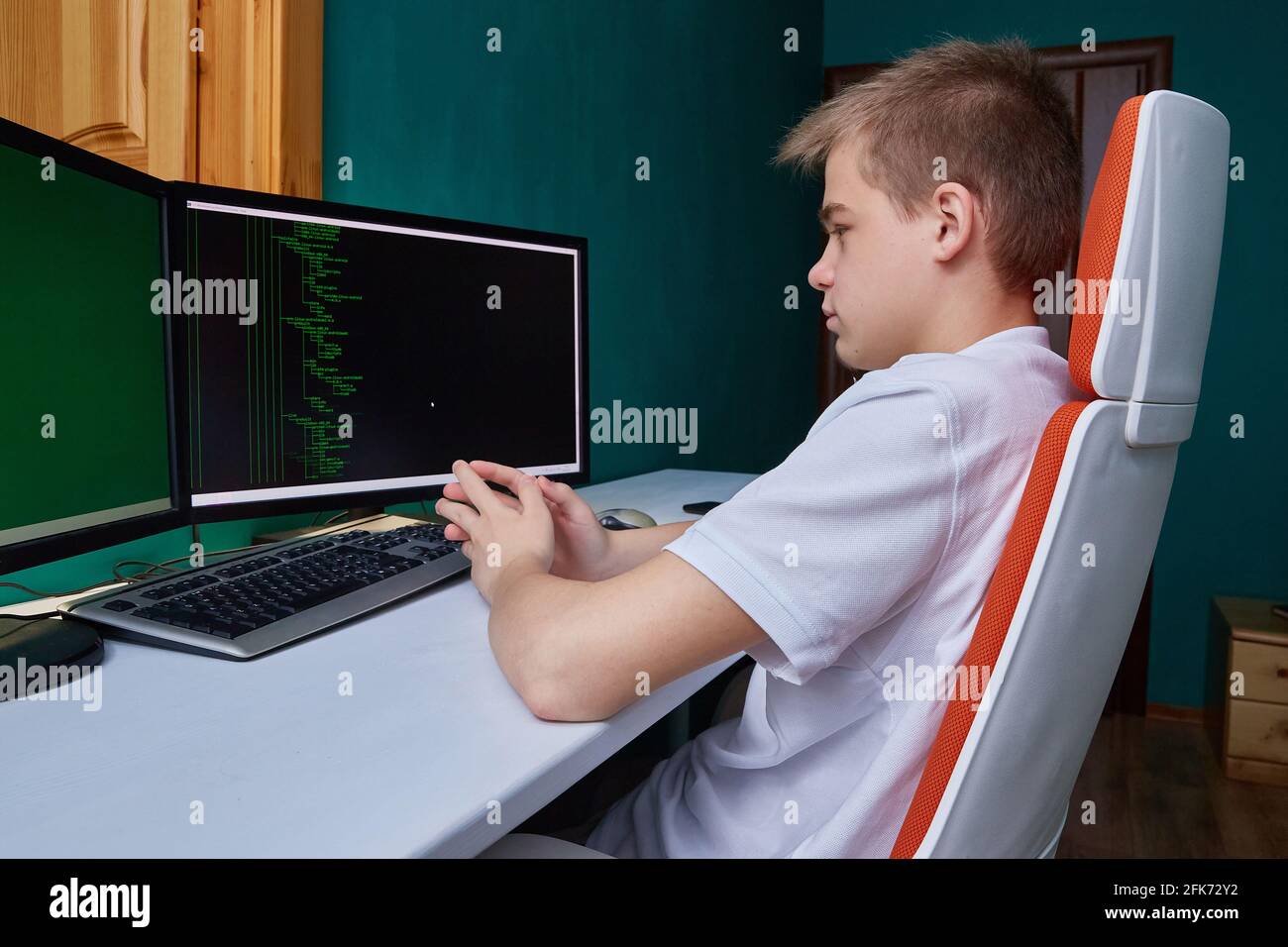 Un estudiante programador de computadora se sienta en una computadora en su  habitación con escritorio y silla para ordenador Fotografía de stock - Alamy
