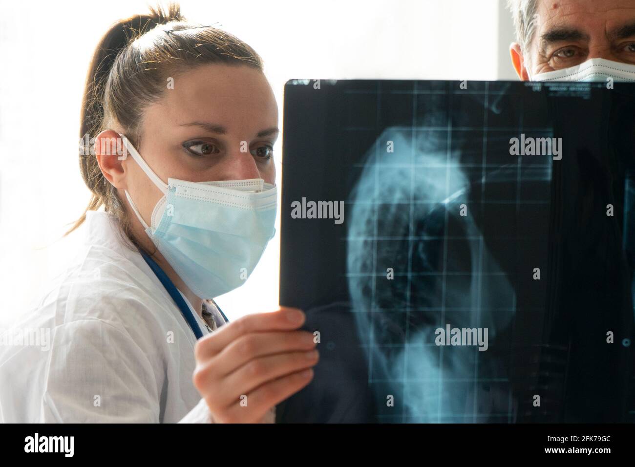 Una joven doctora con un médico de cabecera revisa una radiografía. Concepto de colaboración entre médicos jóvenes y médicos experimentados. Foto de stock