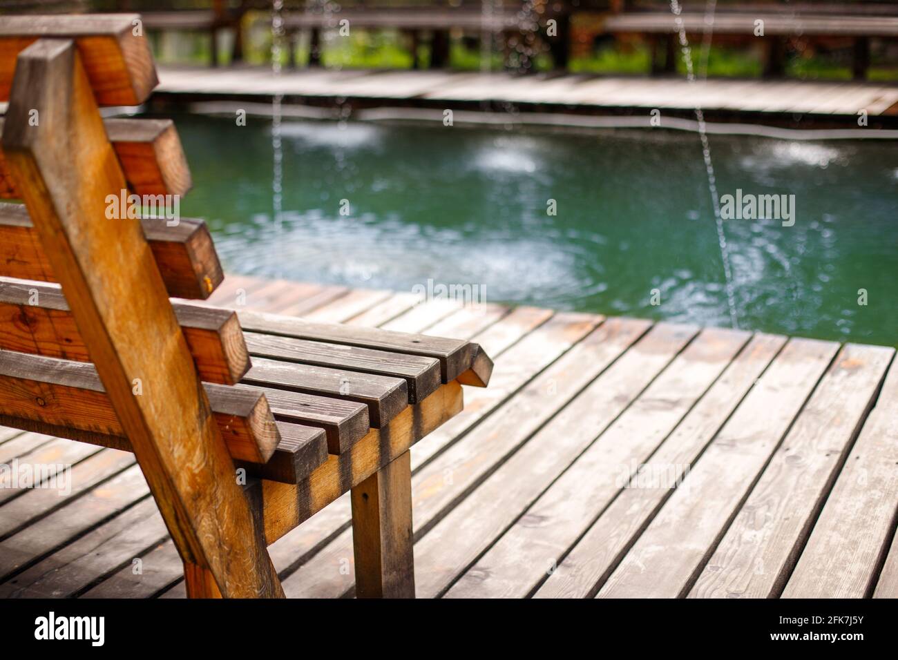 Vista lateral de cerca del banco de madera sobre fondo de la piscina con agua de manantial. Foto de stock