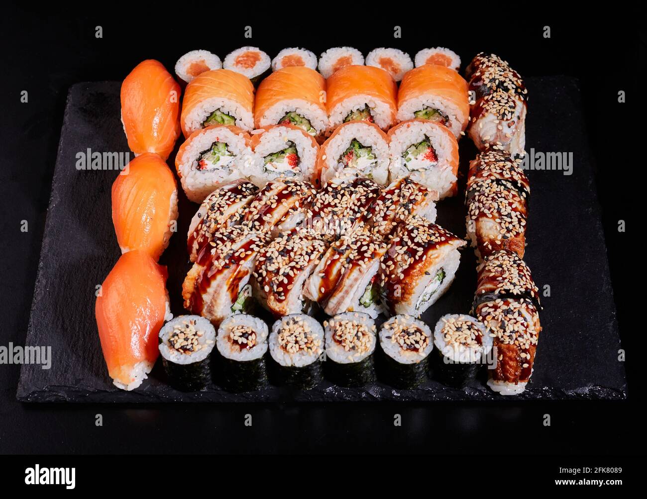 Juego de sushi japonés. Diferentes tipos de apetitosos rollos sobre un plato de piedra sobre fondo negro. Vista superior, diseño plano. Foto de stock