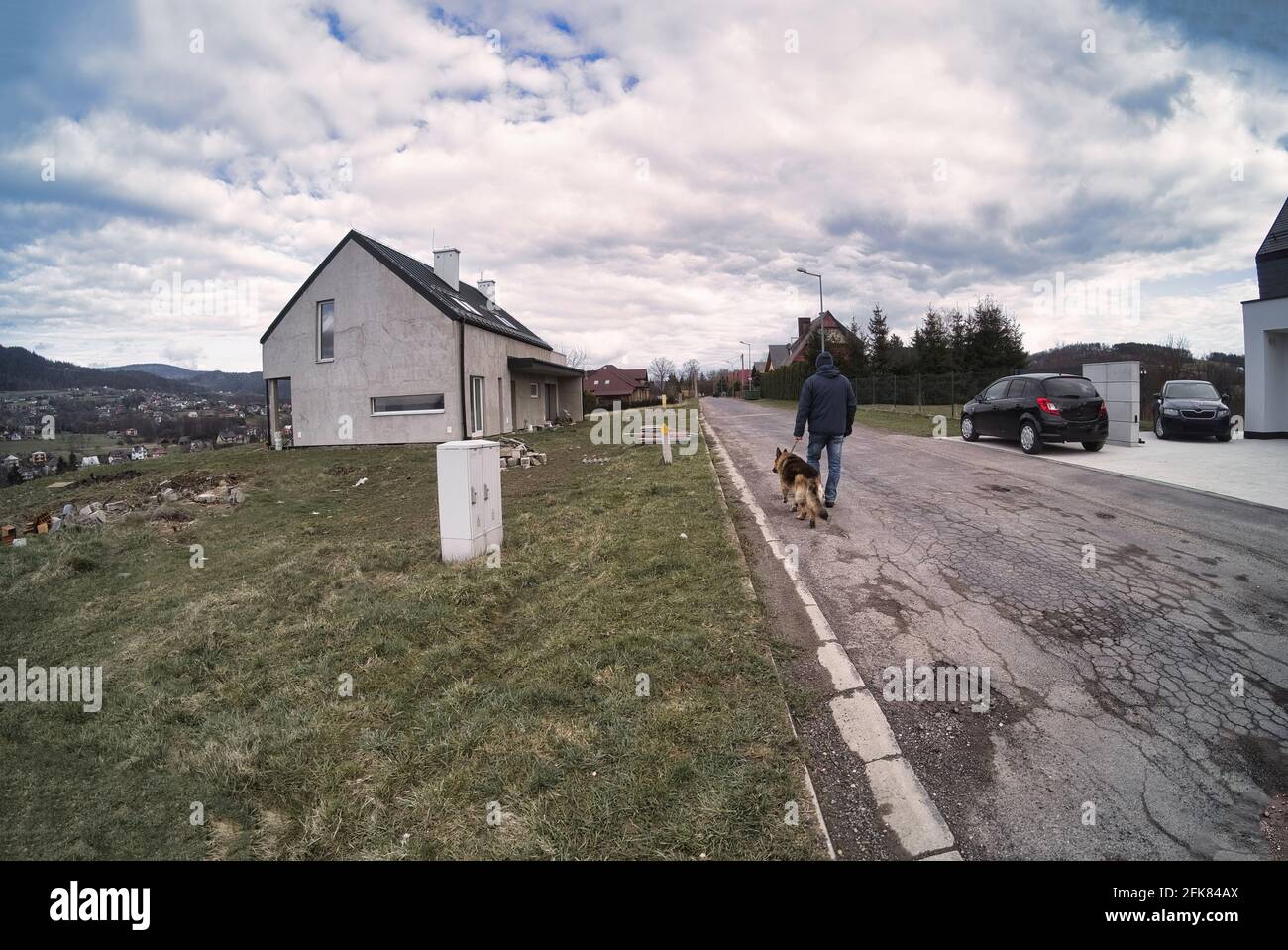 Un hombre con un perro pastor alemán está caminando en el lado de la  carretera en el lado del país. Vista trasera. Un fiel amigo del hombre.  Caminar una larga distancia Fotografía