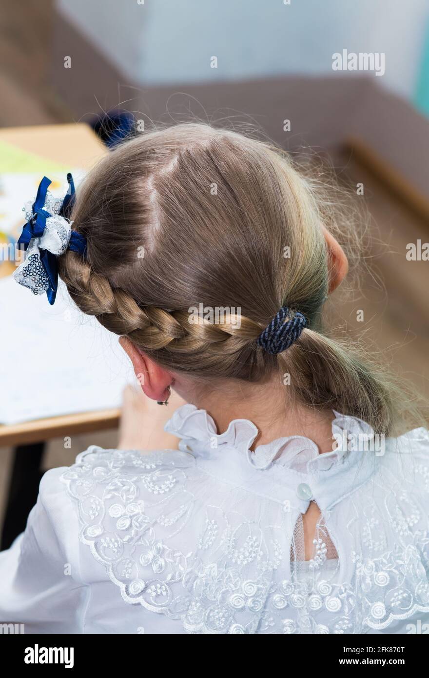 Peinado de una chica con una trenza alrededor de su cabeza y un lazo azul  de cerca. El peinado se hace con horquillas y una banda elástica. Sólo la  parte posterior de