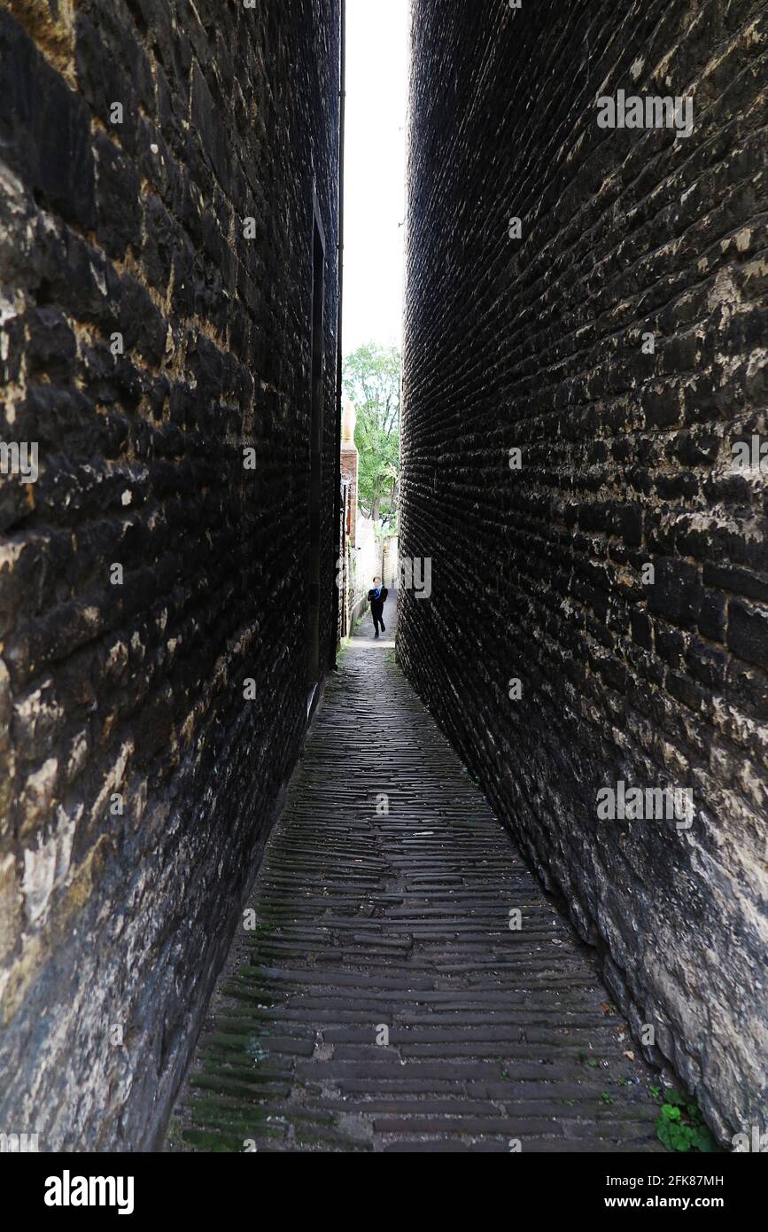 Un niño corre hacia la cámara a lo largo de un estrecho callejón que conduce a St Mary's Street en Stamford, Lincolnshire, Reino Unido. Foto de stock