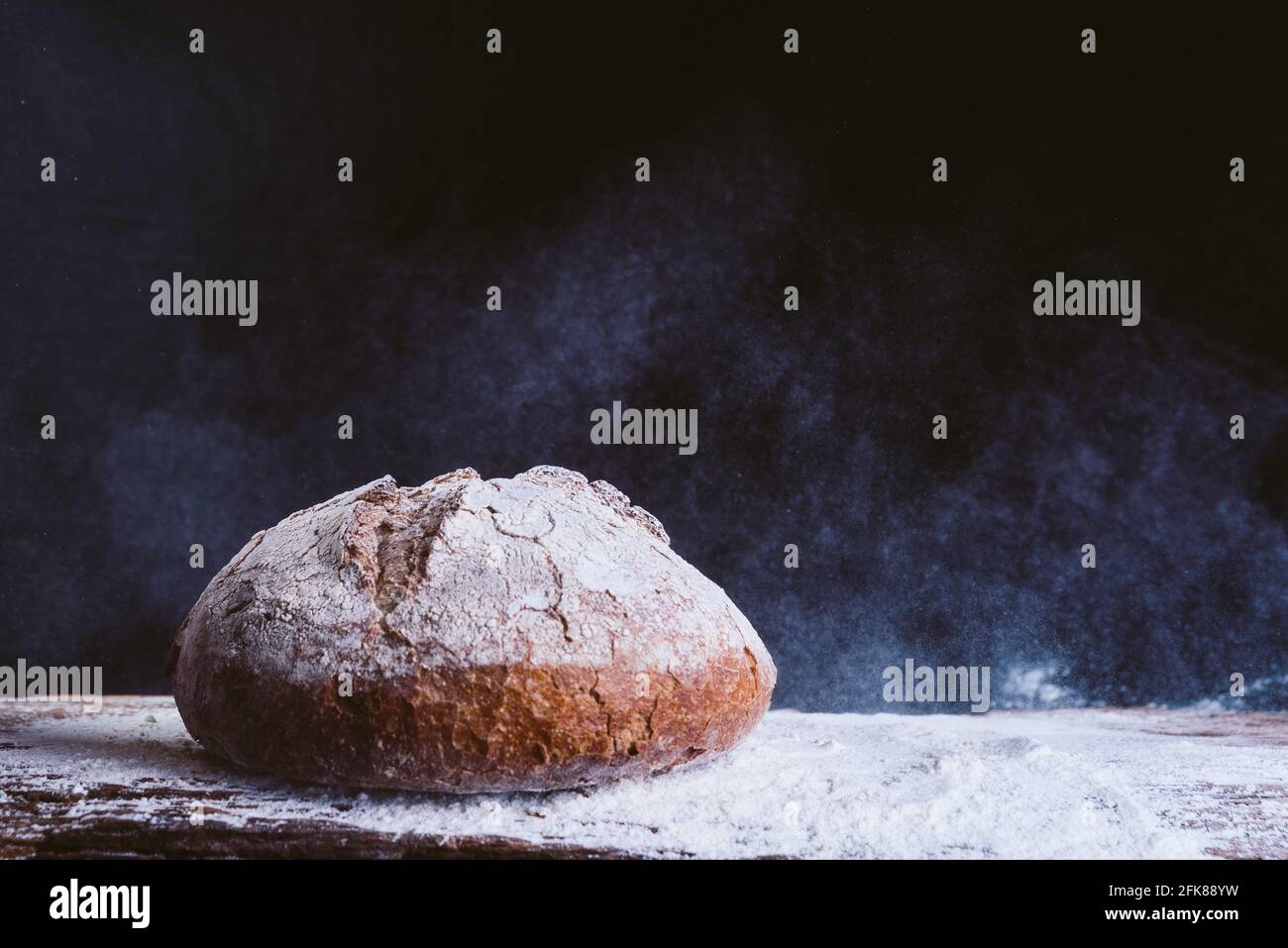 pan dorado fresco y rústico sobre mesa de cocina de madera con polvo de harina sobre fondo negro. concepto de panadería y alimentación saludable Foto de stock