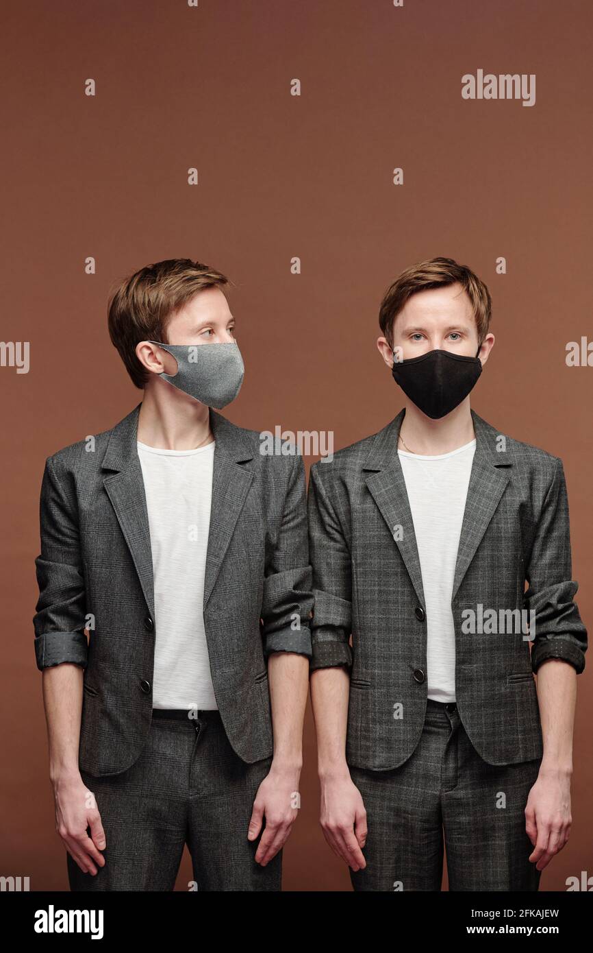 Hombre joven con traje elegante sport de pie sobre fondo marrón y mirando a  hermano gemelo en máscara negra Fotografía de stock - Alamy