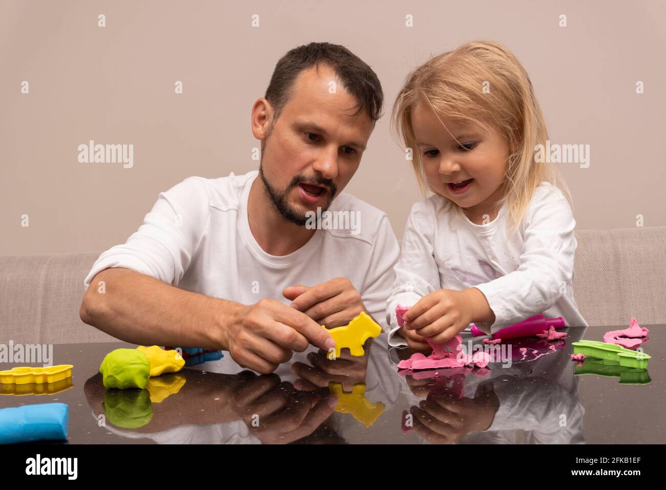 El joven hombre caucásico juega con su hija haciendo animales coloridos de masa playera Foto de stock