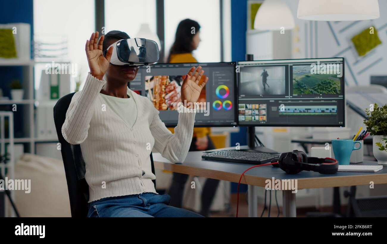 Editor de vídeo africano experimentando gafas VR, gesturing, edición de  montaje de película de vídeo trabajando con material de archivo y sonido en  la computadora con dos pantallas. Videógrafo procesando la película