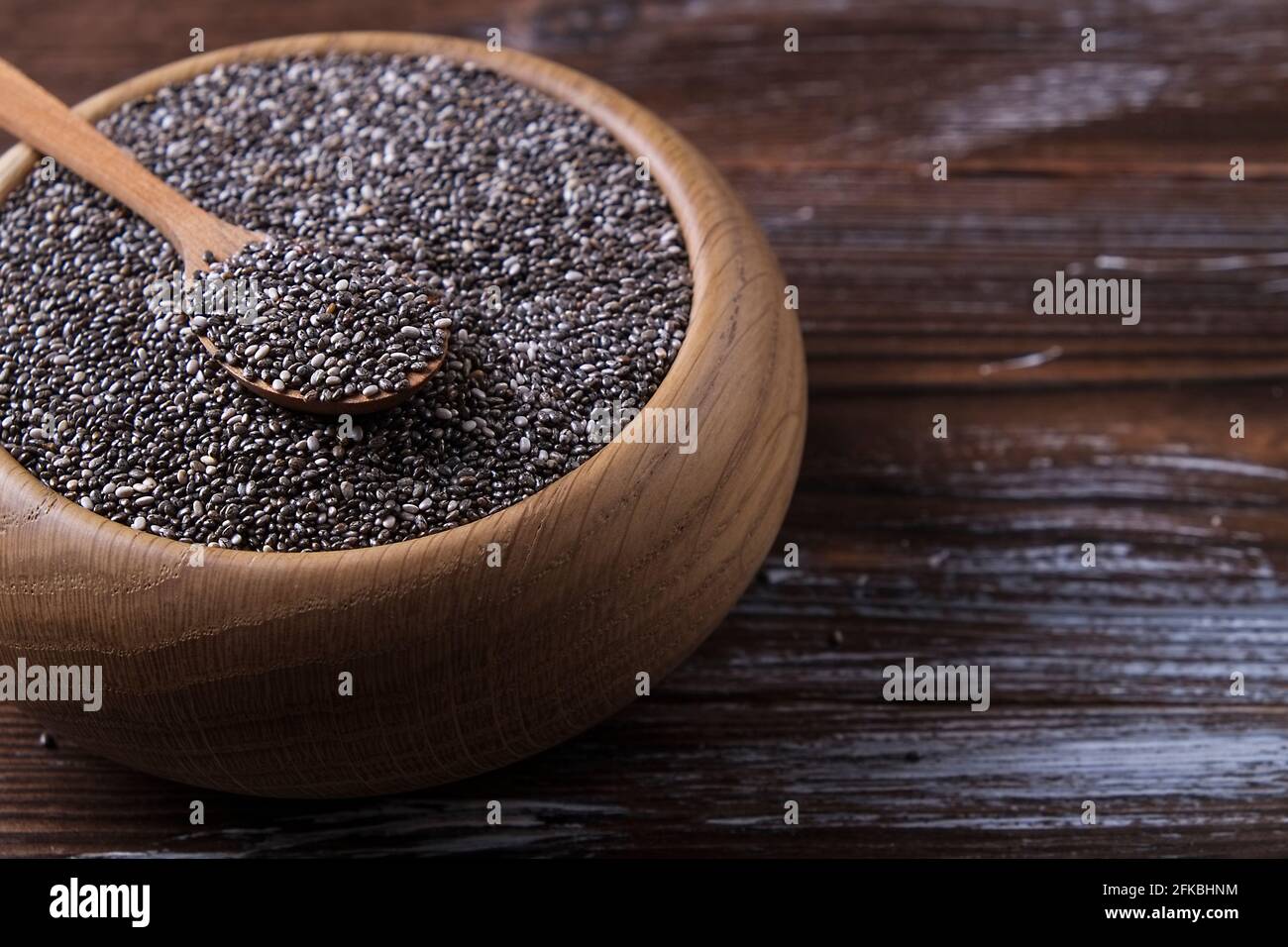 Vista superior del tazón de madera con pila de semillas de chía negra orgánica y cuchara sobre mesa texturizada de madera rallada. Alimentación vegana sana y nutritiva. CLEA Foto de stock