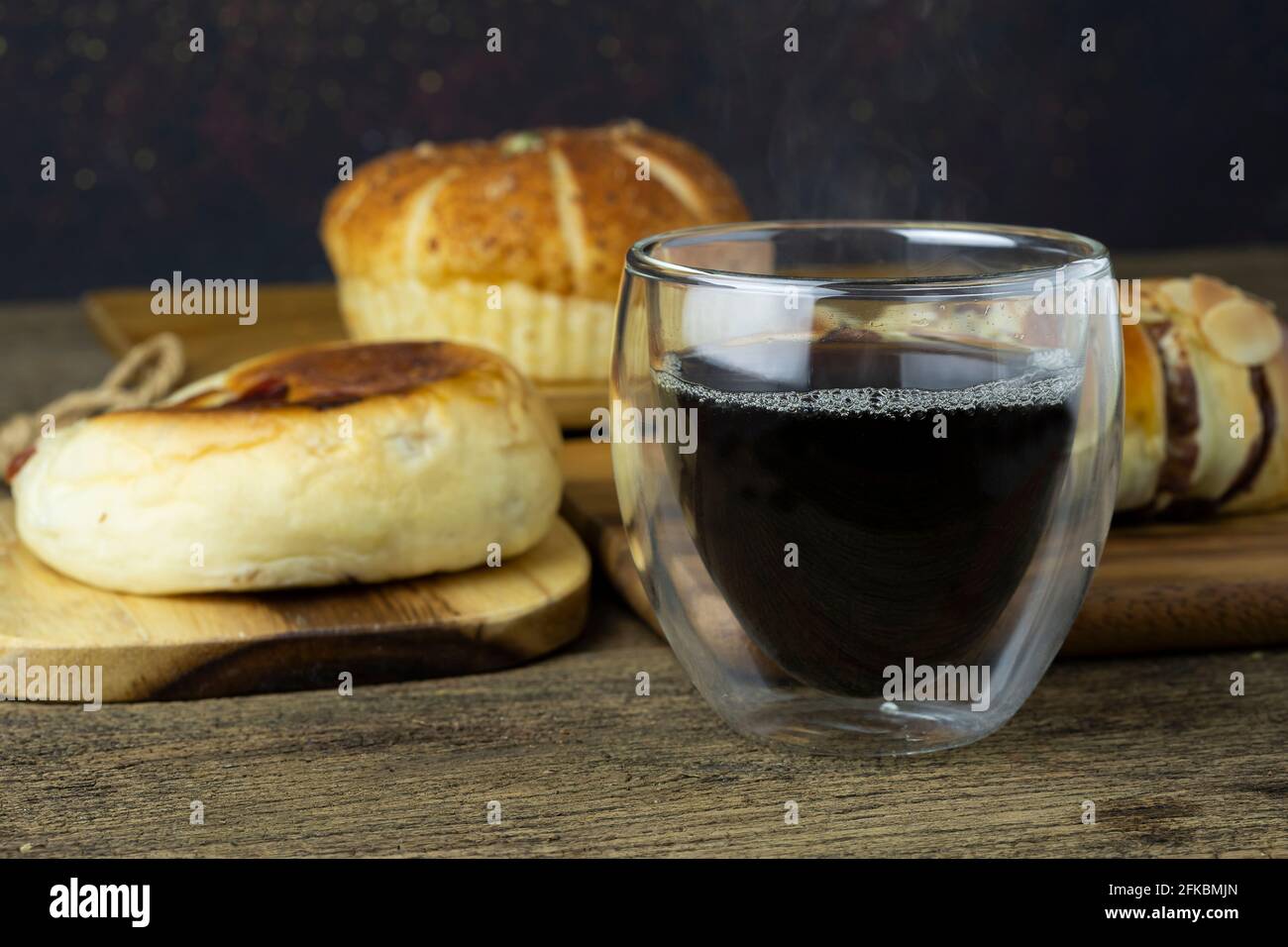 Café negro caliente se coloca en la mesa de madera, hay pan en el fondo. Foto de stock
