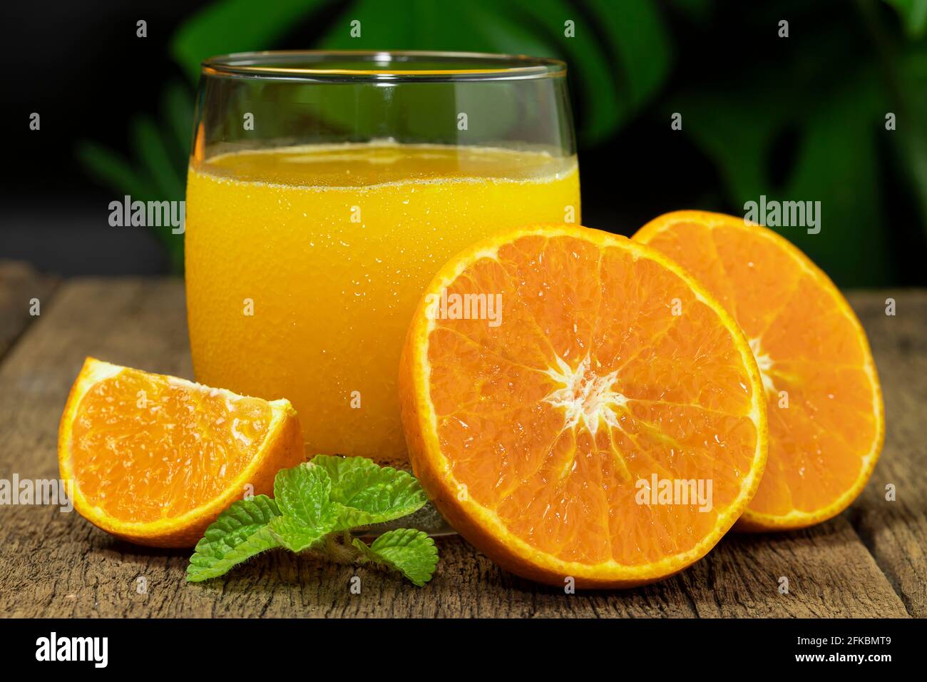 Un vaso de zumo de naranja y fruta de naranja cortado a la mitad en la mesa de madera. Foto de stock