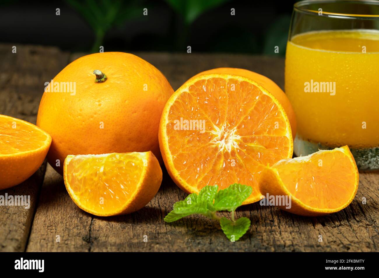 Cierre la fruta naranja cortada por la mitad con una rodaja de naranja y un vaso de zumo de naranja sobre la mesa de madera. Foto de stock