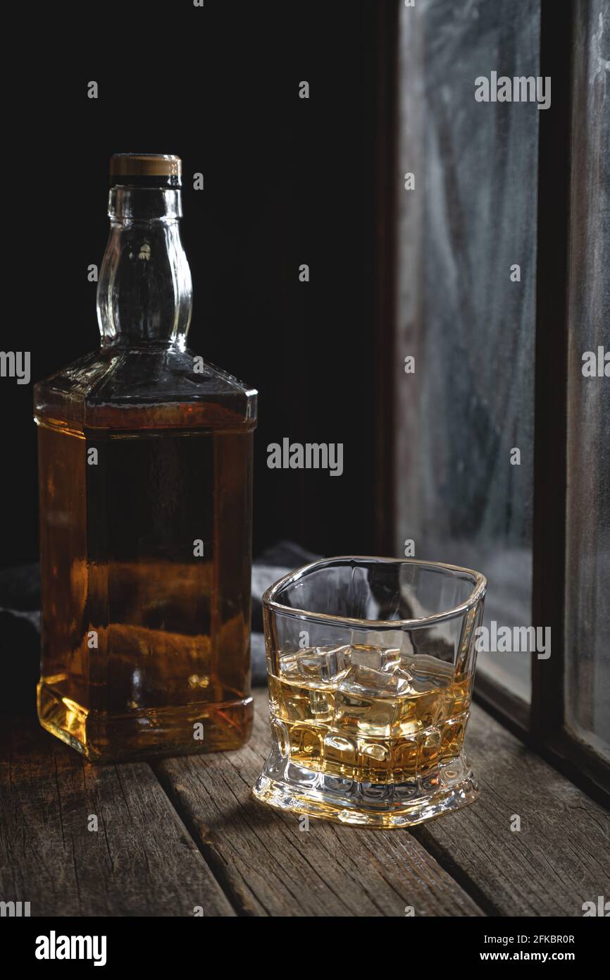 Vaso de whisky con hielo y botella junto a la ventana sobre una mesa  rústica de madera Fotografía de stock - Alamy