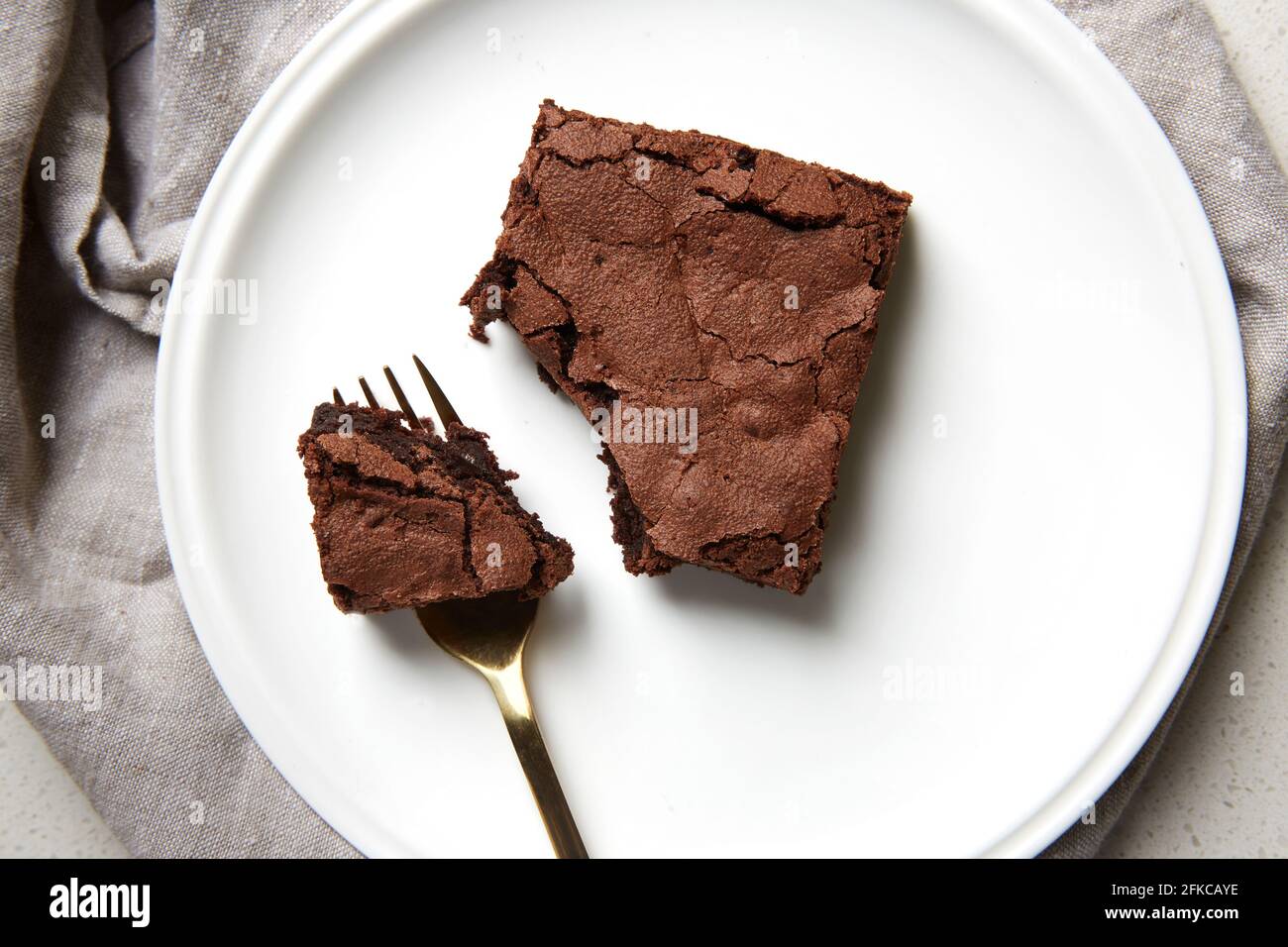 Vista superior de una pieza de brownie fresca en un plato blanco con  cubiertos de oro y ropa de cama gris Fotografía de stock - Alamy