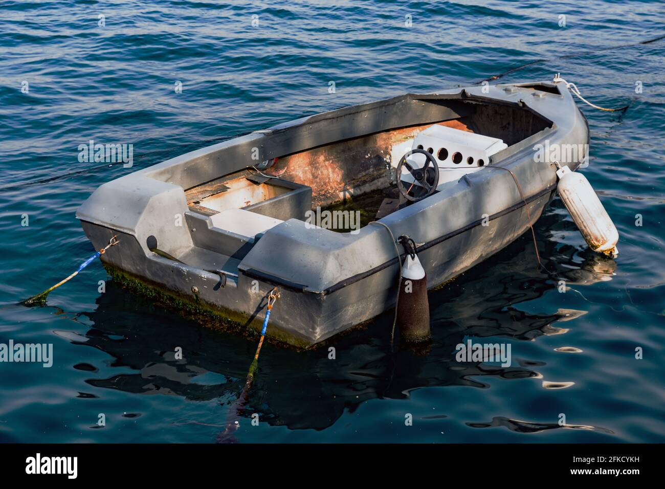 Barco abandonado de fibra de vidrio sin motor ni rotor, anclado en el mar, con sombras y luz del sol. Foto de stock