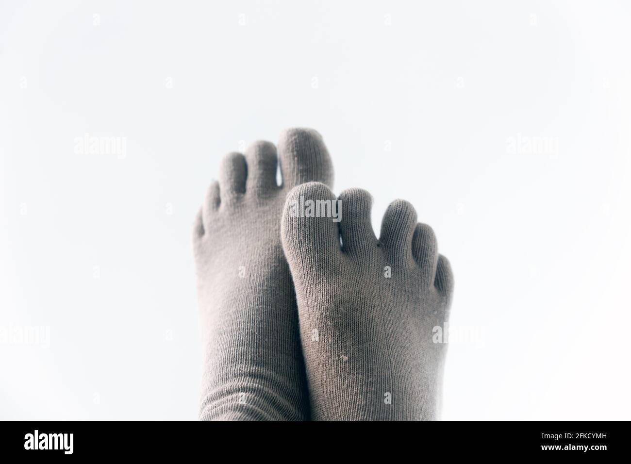 Un par de pies usando calcetines para los dedos, cruzados, aislados sobre fondo blanco. Foto de stock