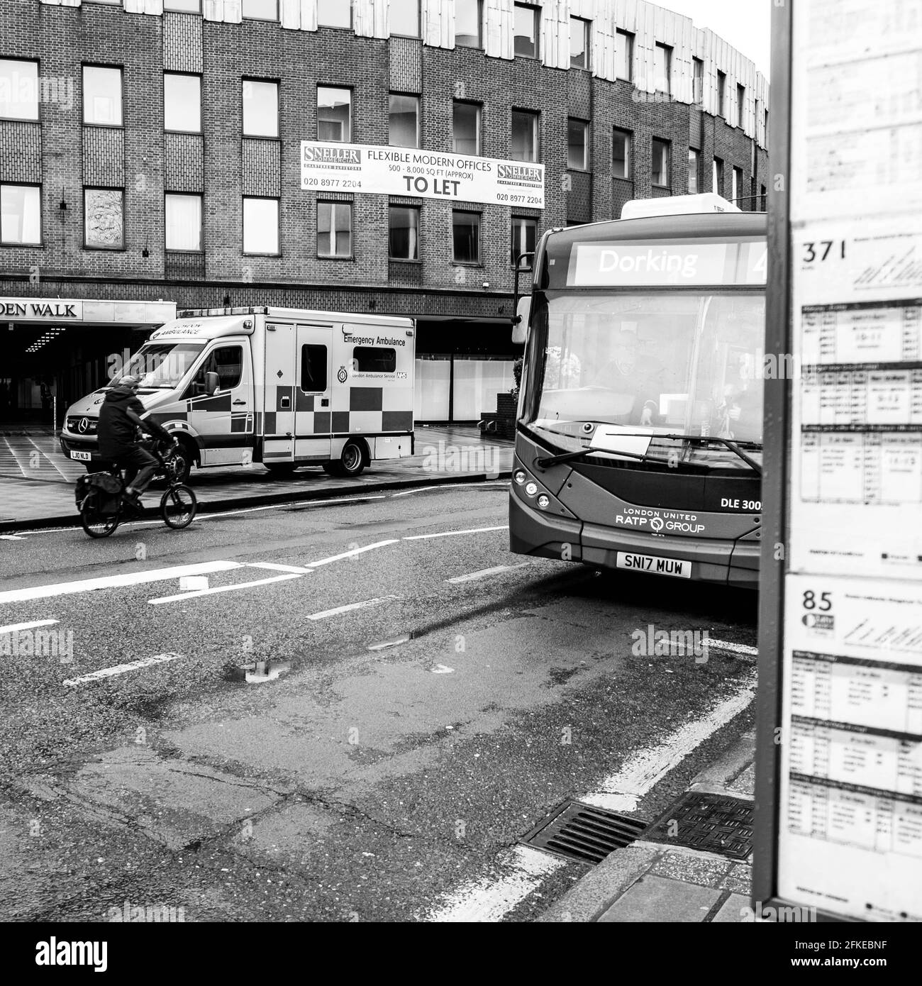 Kingston Upon Thames, Londres Reino Unido, Cyclist pasando UN autobús estacionado de ambulancia y transporte público en una calle alta vacía Foto de stock