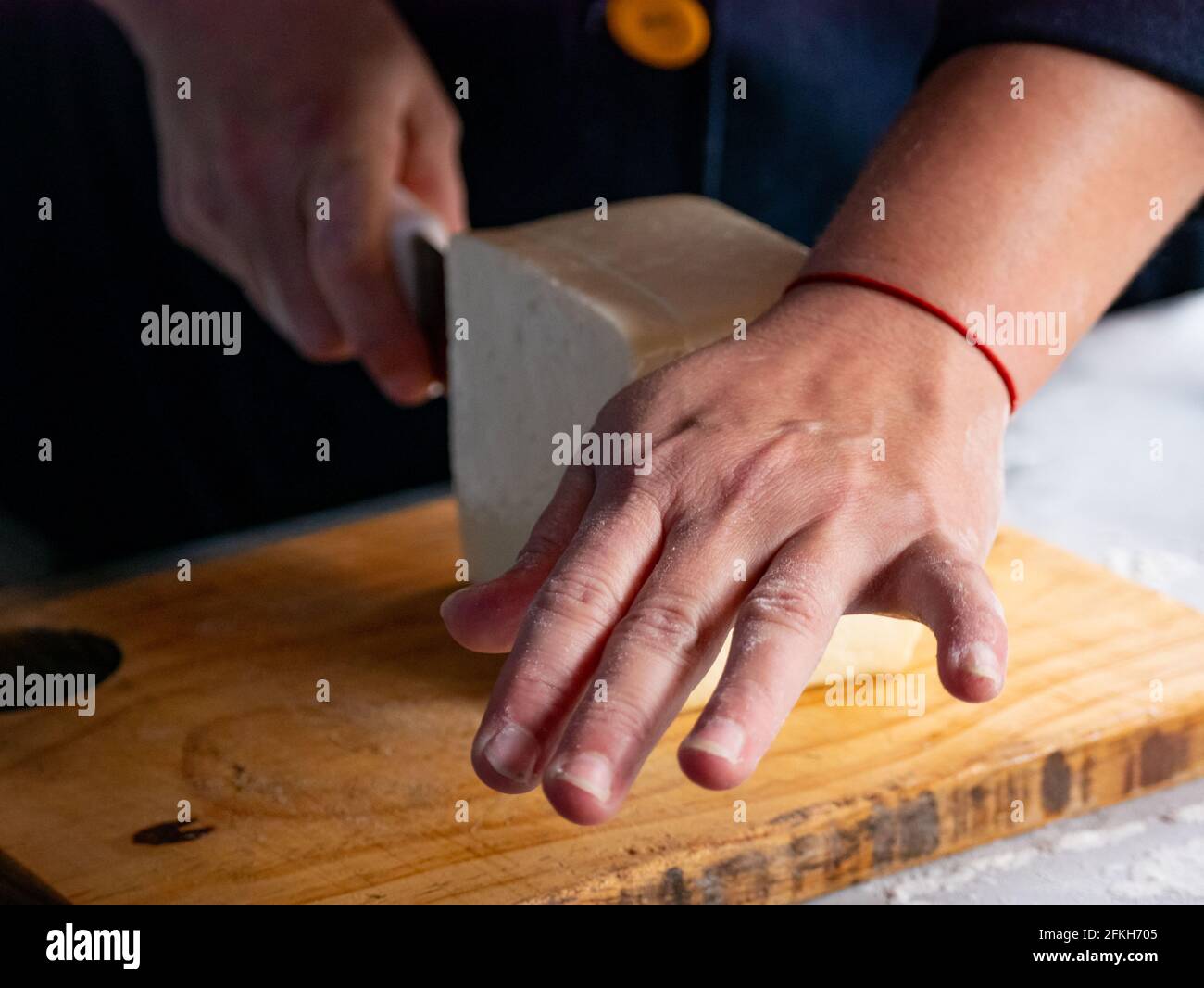 Las manos de la mujer cortando el queso en una mesa de madera en el Tabla de metal Foto de stock