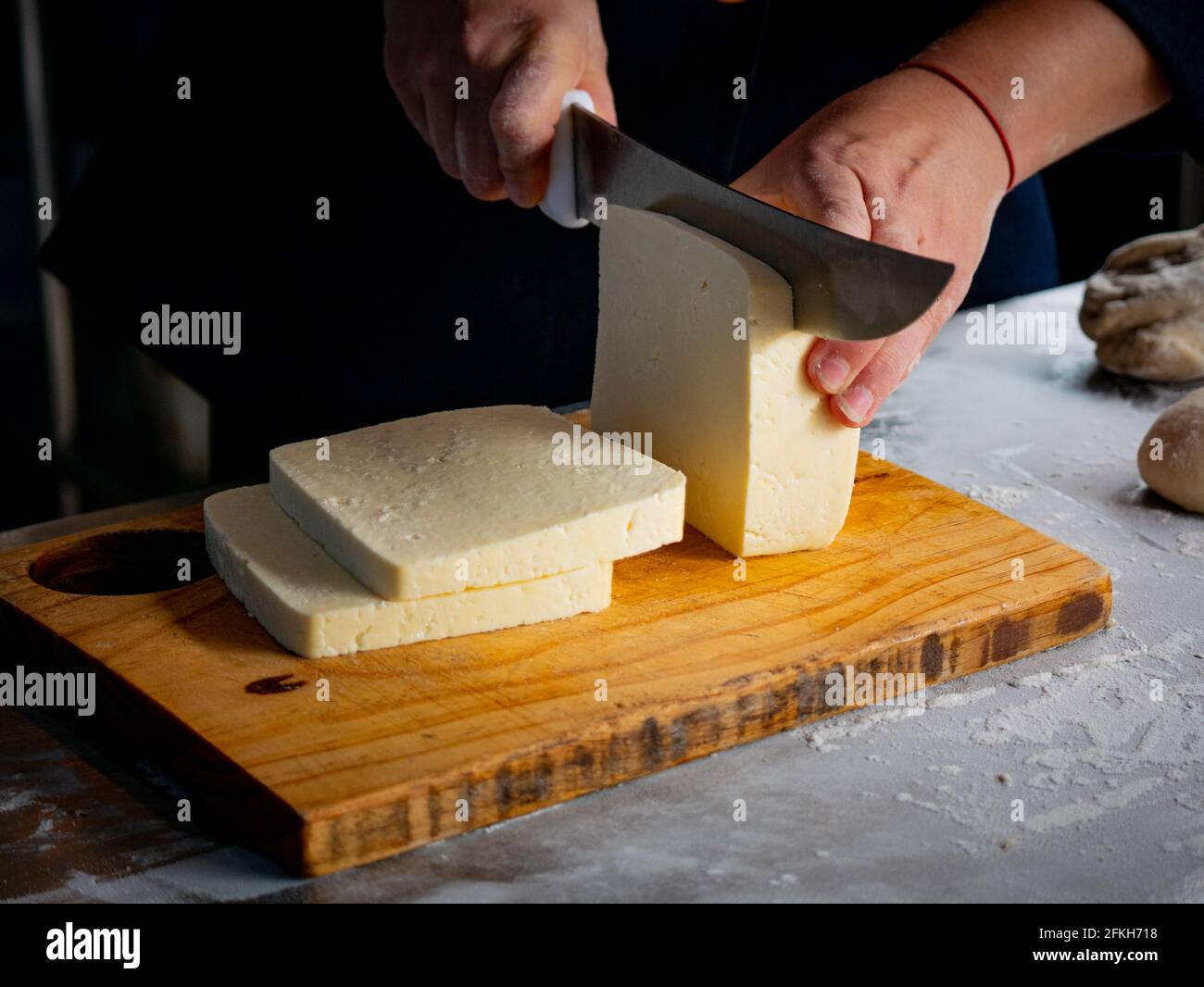 Las manos de la mujer cortando el queso en una mesa de madera en el Tabla de metal Foto de stock