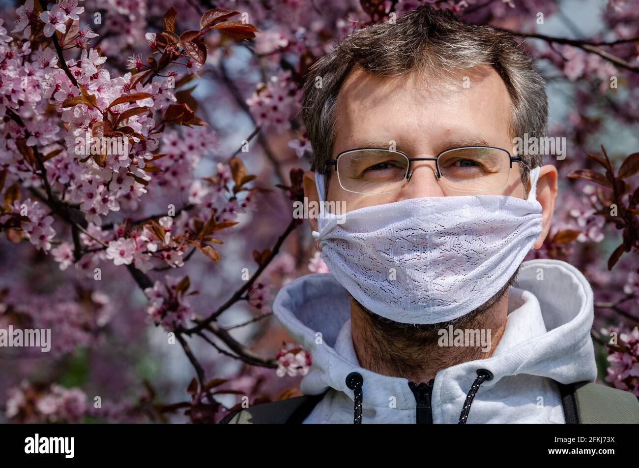 Retrato de un hombre de mediana edad en un protector hecho a sí mismo máscara bajo un cerezo en flor durante la pandemia de covid Foto de stock