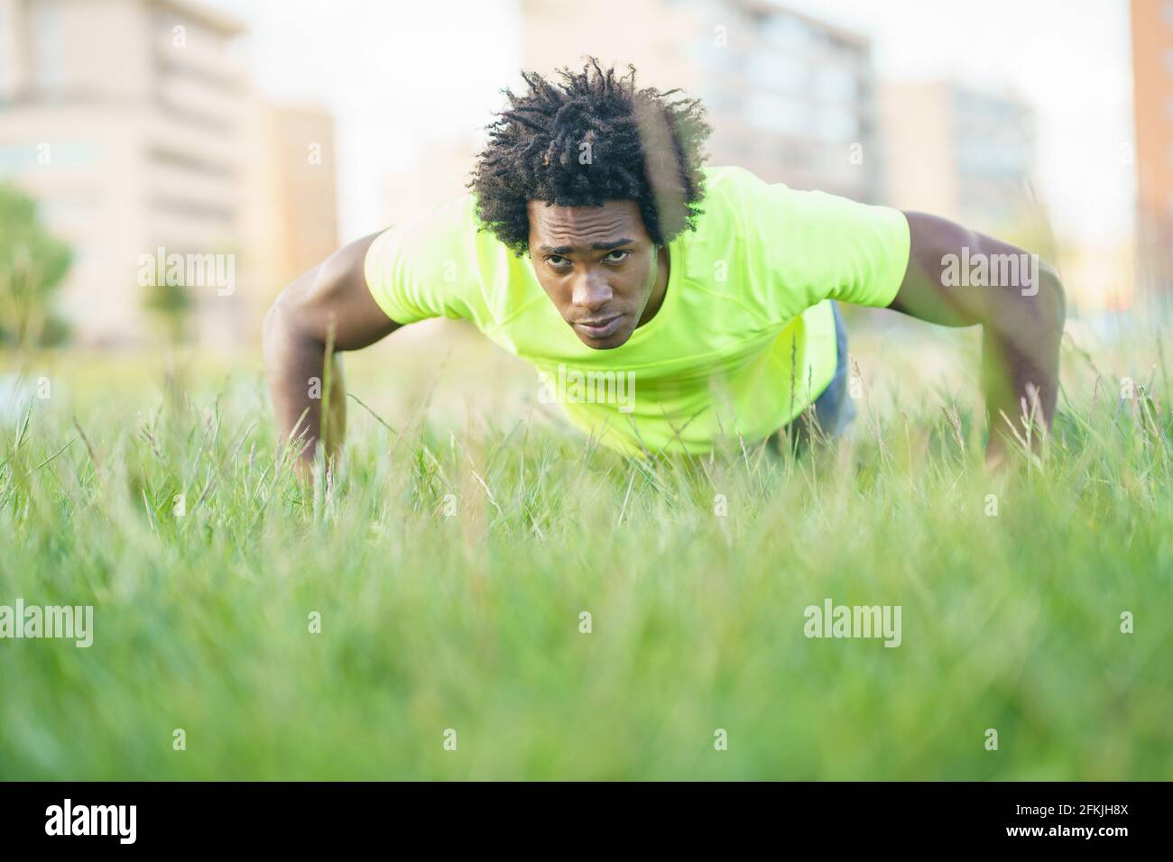 Hombre negro haciendo flexiones ejercitando su pecho en la hierba de un parque urbano. Foto de stock