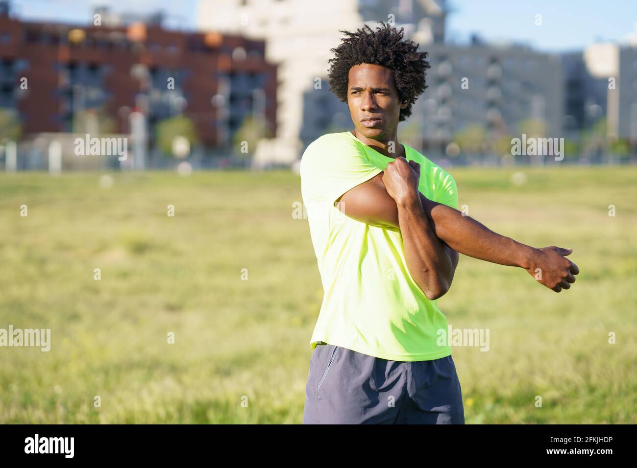 Hombre negro con pelo afro que se estira después de correr al aire libre. Foto de stock