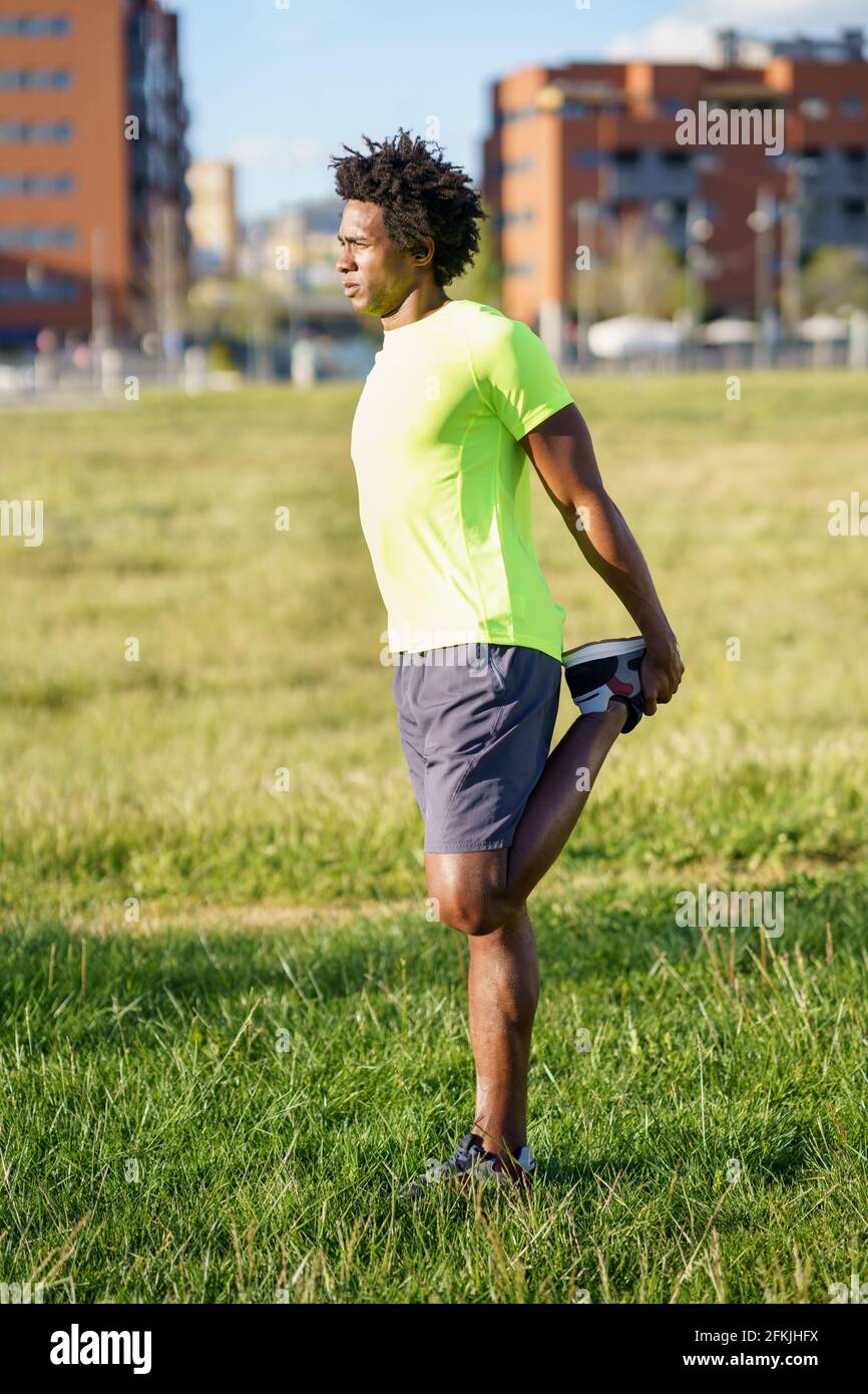 Hombre negro estirando sus cuadriceps después de correr al aire libre. Foto de stock