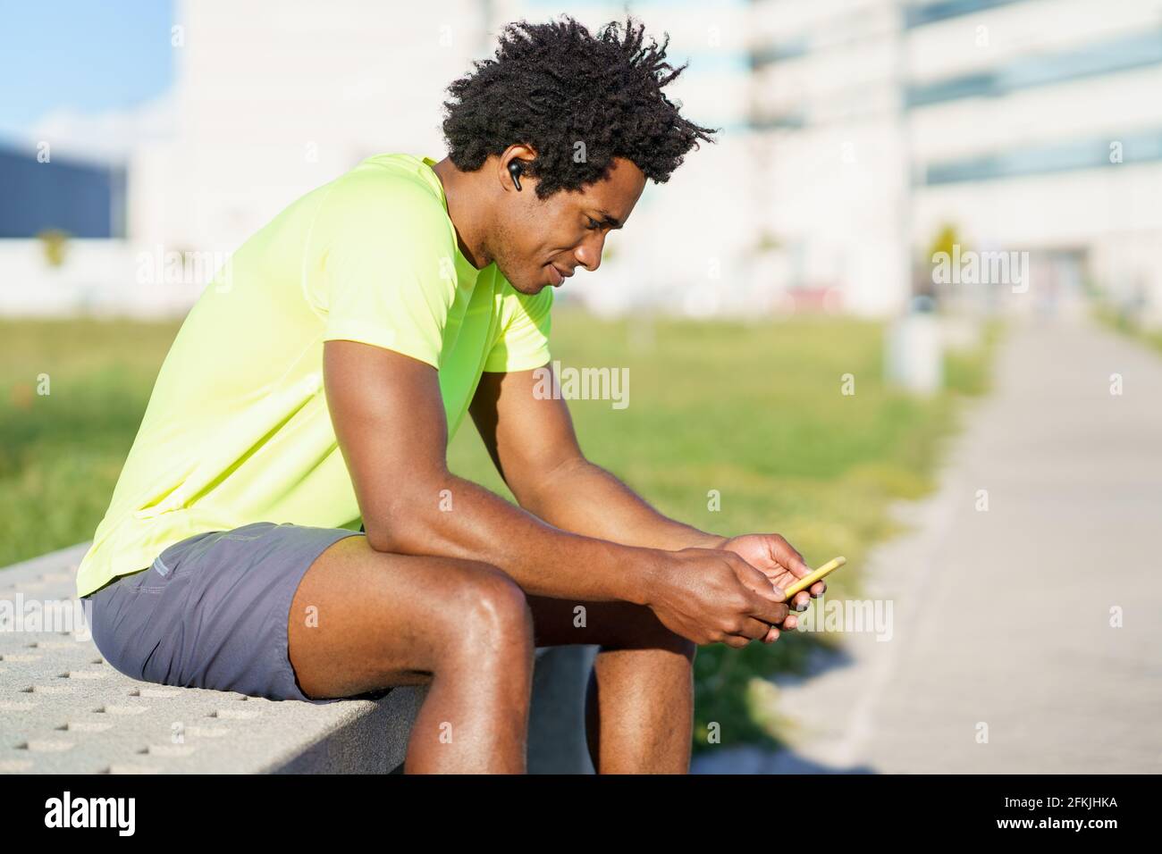 Hombre negro consultando su smartphone con alguna aplicación de ejercicio mientras descansa de su entrenamiento. Foto de stock