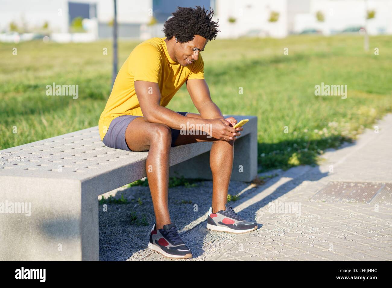 Hombre negro consultando su smartphone con alguna aplicación de ejercicio mientras descansa de su entrenamiento. Foto de stock