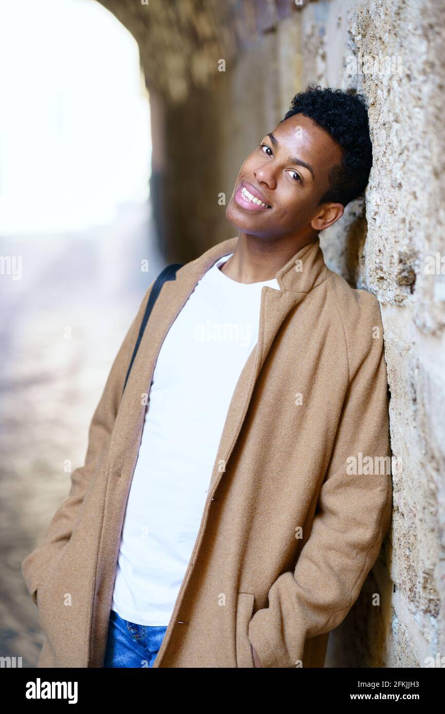 Hombre negro joven mirando la cámara con una mirada feliz y esperanzada en su cara al aire libre. Foto de stock