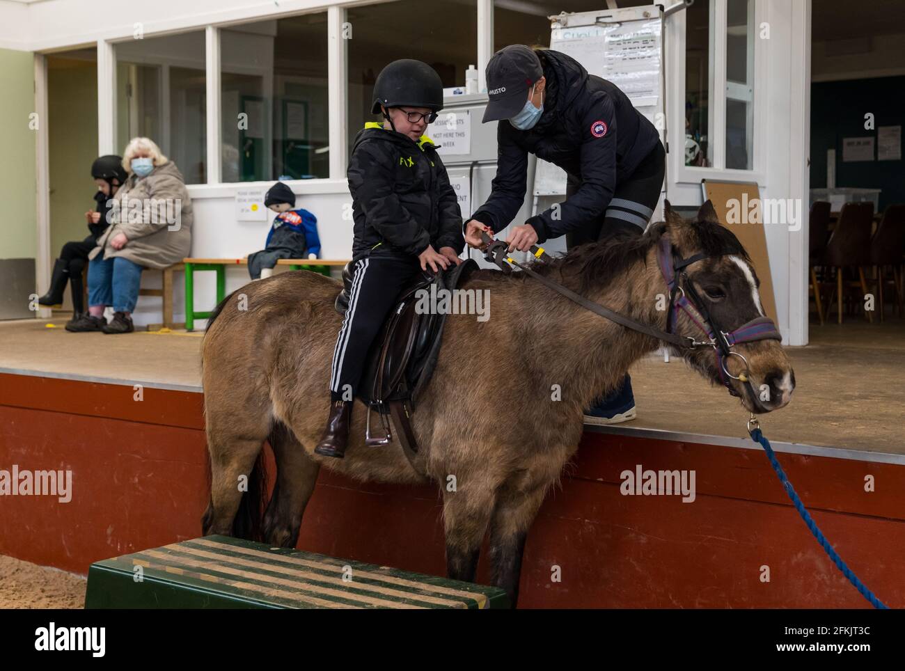 Niño con síndrome de Down subiendo a caballo, montando para discapacitados en Muirfield Riding Therapy, East Lothian, Escocia, Reino Unido Foto de stock