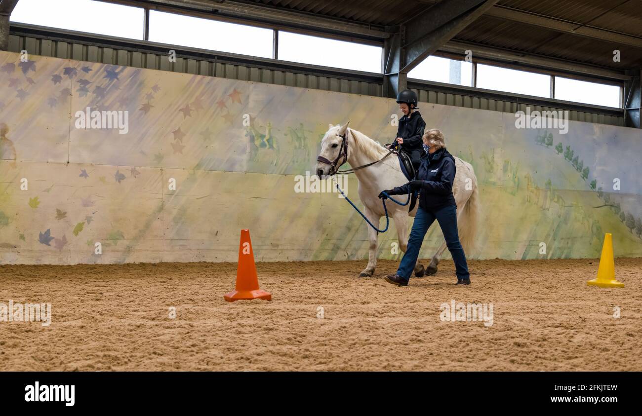 Niño montando caballo blanco aprendiendo control de las riendas, Equitando para discapacitados en Muirfield Riding Therapy, East Lothian, Escocia, Reino Unido Foto de stock