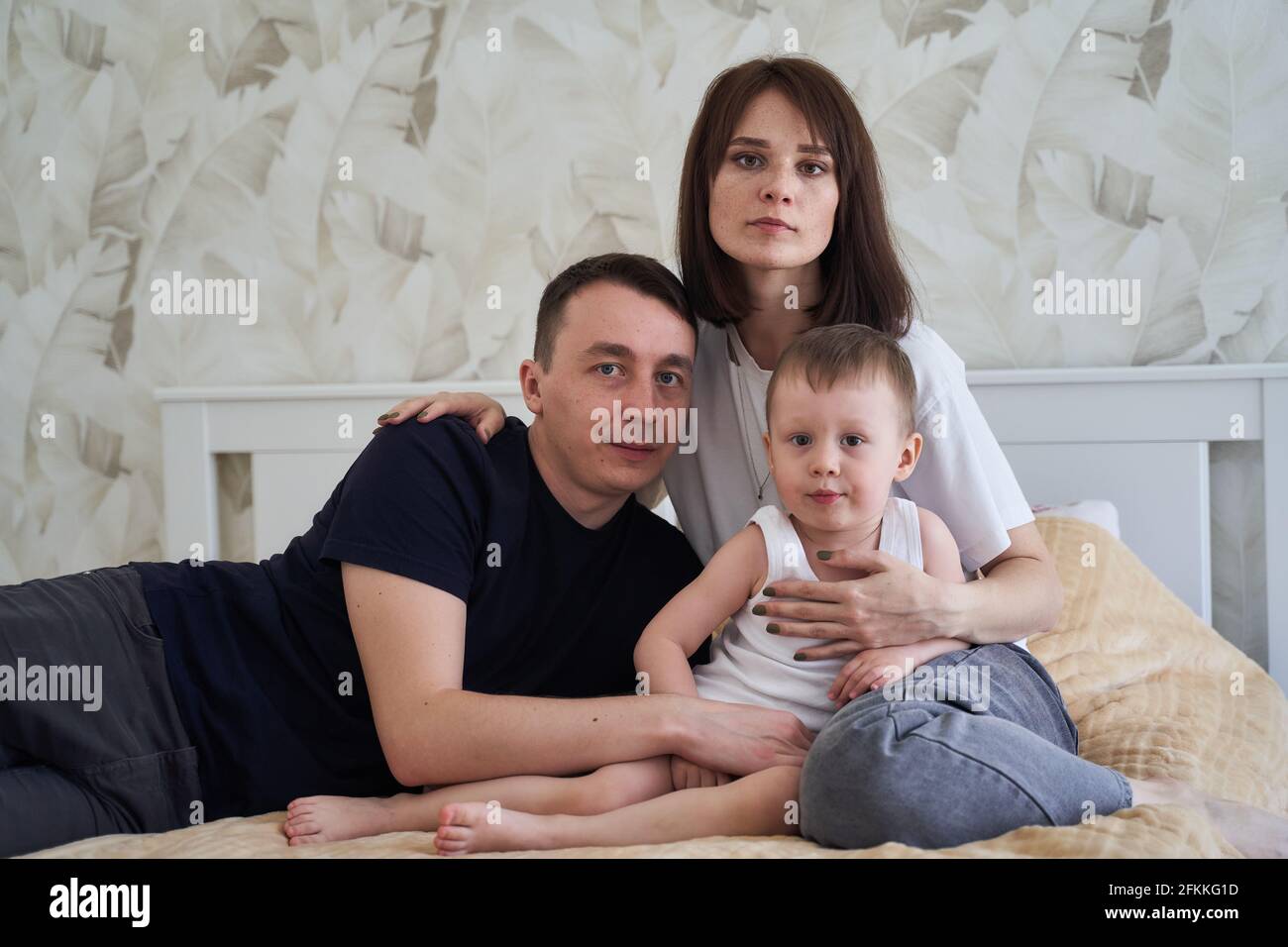 mamá papá y bebé se sientan en la cama en casa Foto de stock