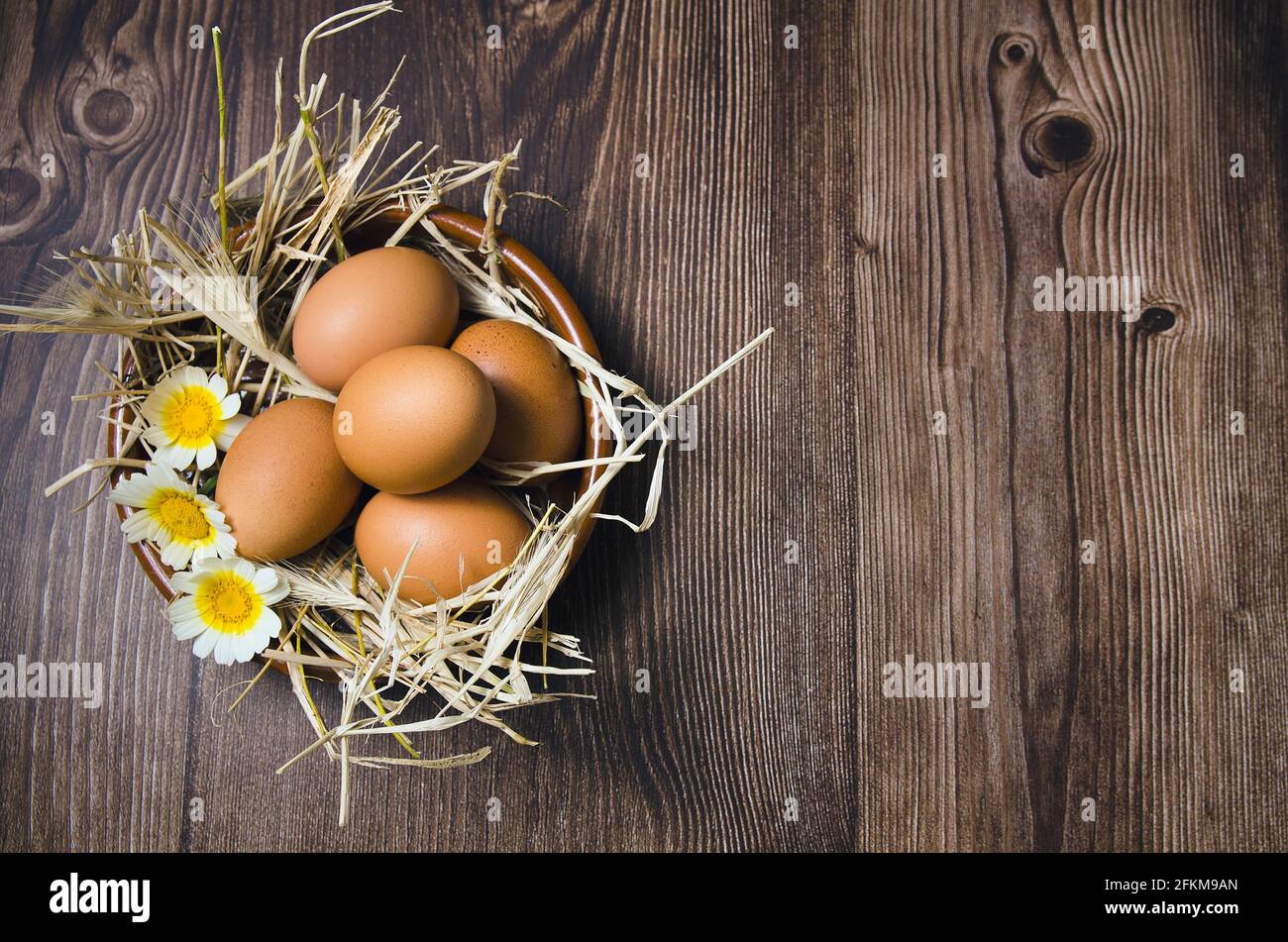 Huevos marrones sobre mesa de madera con flores Foto de stock