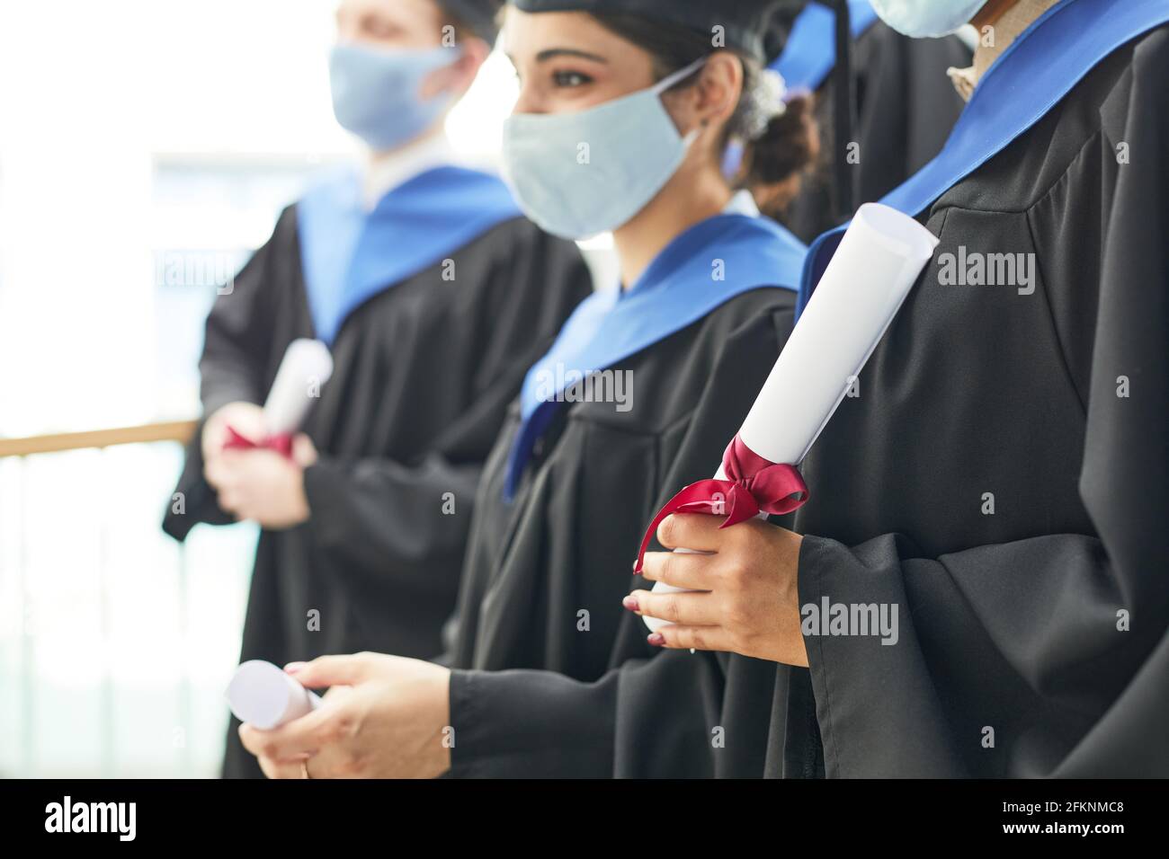Vista lateral de diversos grupos de jóvenes que llevan graduación batas y máscaras mientras están de pie en fila Foto de stock