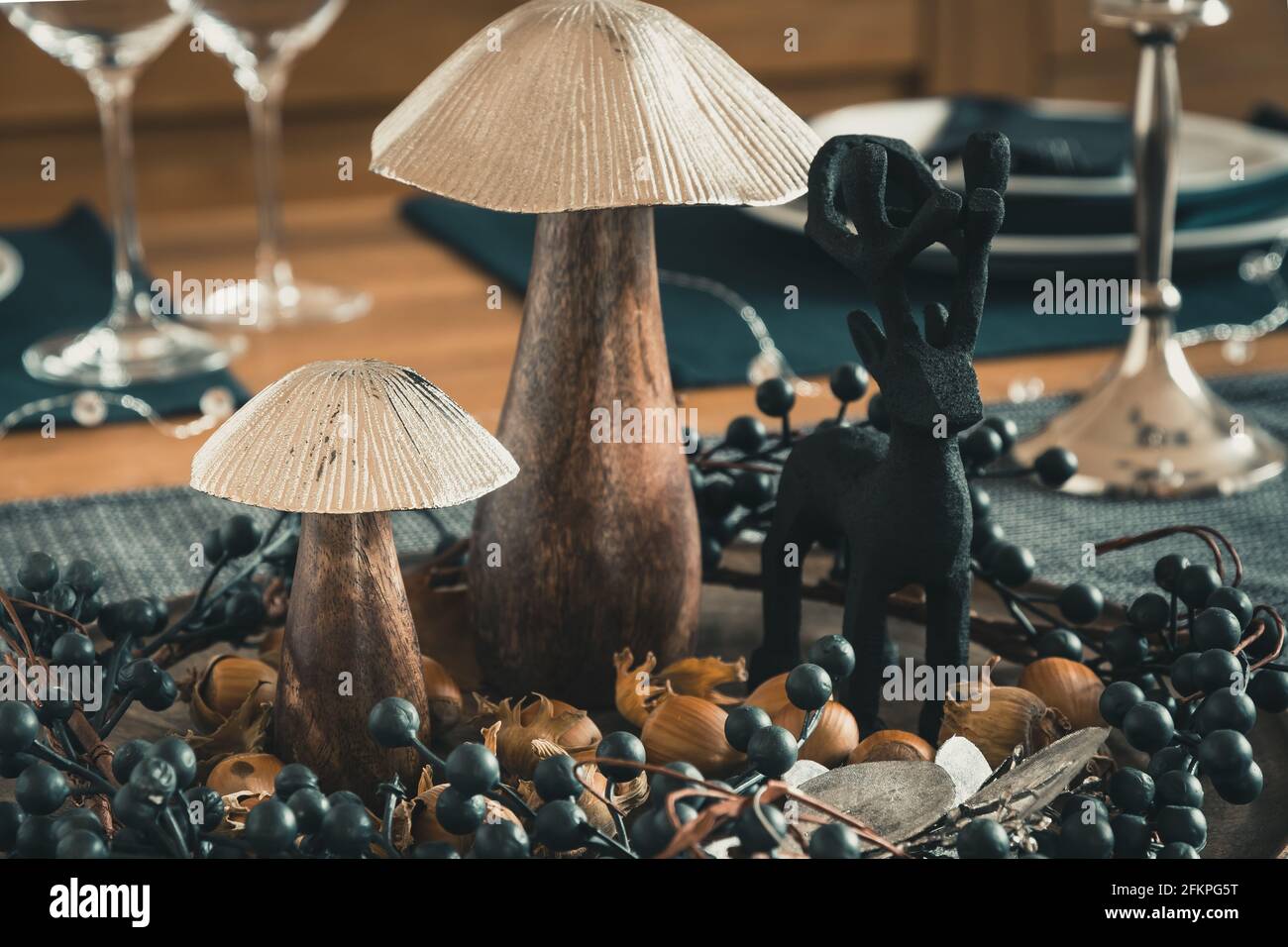 Primer plano de la decoración de la mesa otoñal con setas de madera, corona de bayas, avellanas y ciervos de madera, dominados por colores azul oscuro, plata y madera Foto de stock