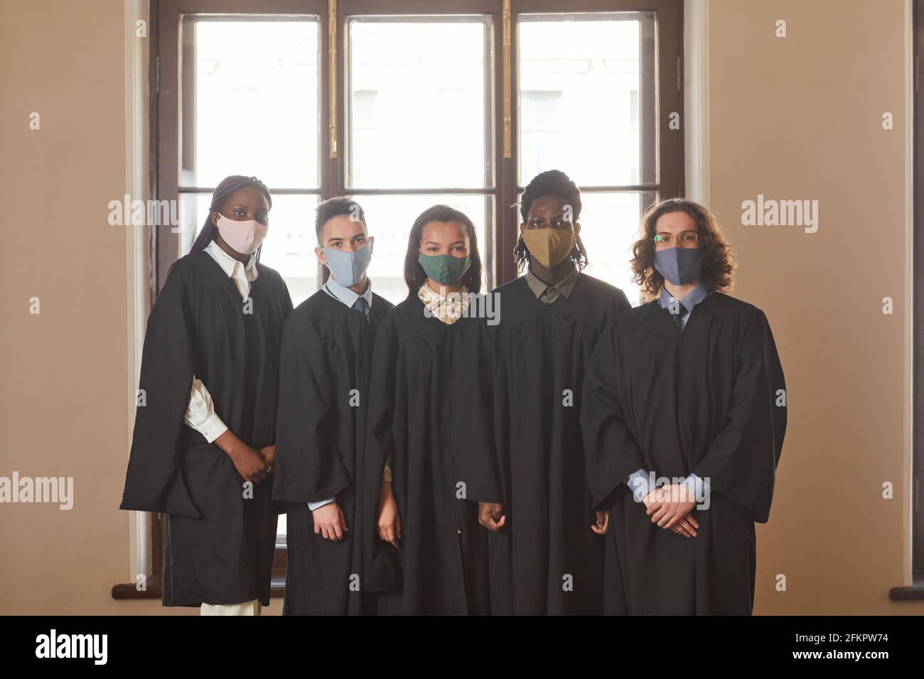 Grupo diverso de jóvenes que llevan máscaras y ceremonial negro batas durante la ceremonia de graduación en la pandemia de covid Foto de stock