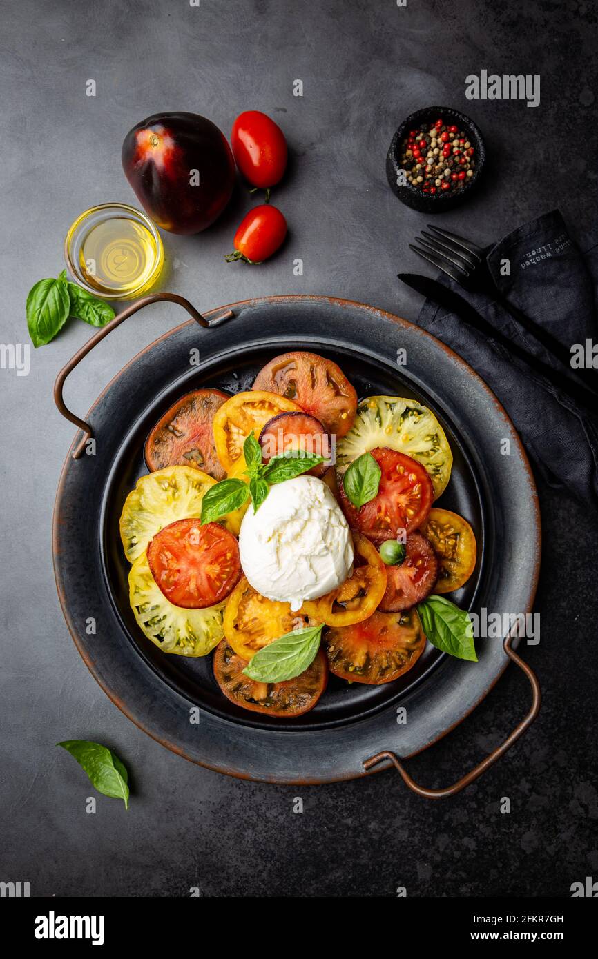 Deliciosa ensalada Caprese con tomates coloridos maduros y queso mozzarella con hojas frescas de albahaca. Comida italiana, vista superior Foto de stock