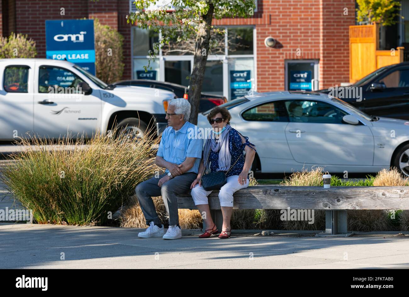 Vista de la calle de la pareja mayor sentada en el banco en el callejón de la ciudad disfrutando de buen tiempo Foto de stock