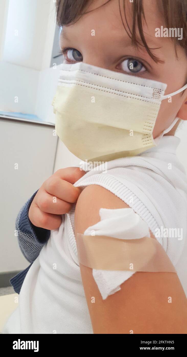 Triste y con dolor niño niño muestra su brazo después de la vacunación. Máscara facial cubierta. Foto de stock