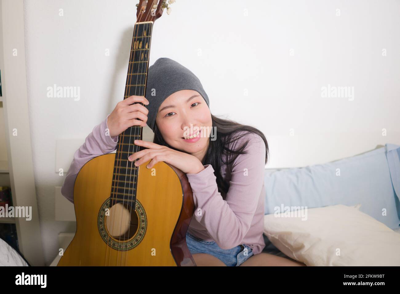 Joven mujer asiática feliz tocando la guitarra en la cama - atractivo Y  hermosa chica coreana en la habitación disfrutando cantando y escribiendo  música relajada en casa Fotografía de stock - Alamy