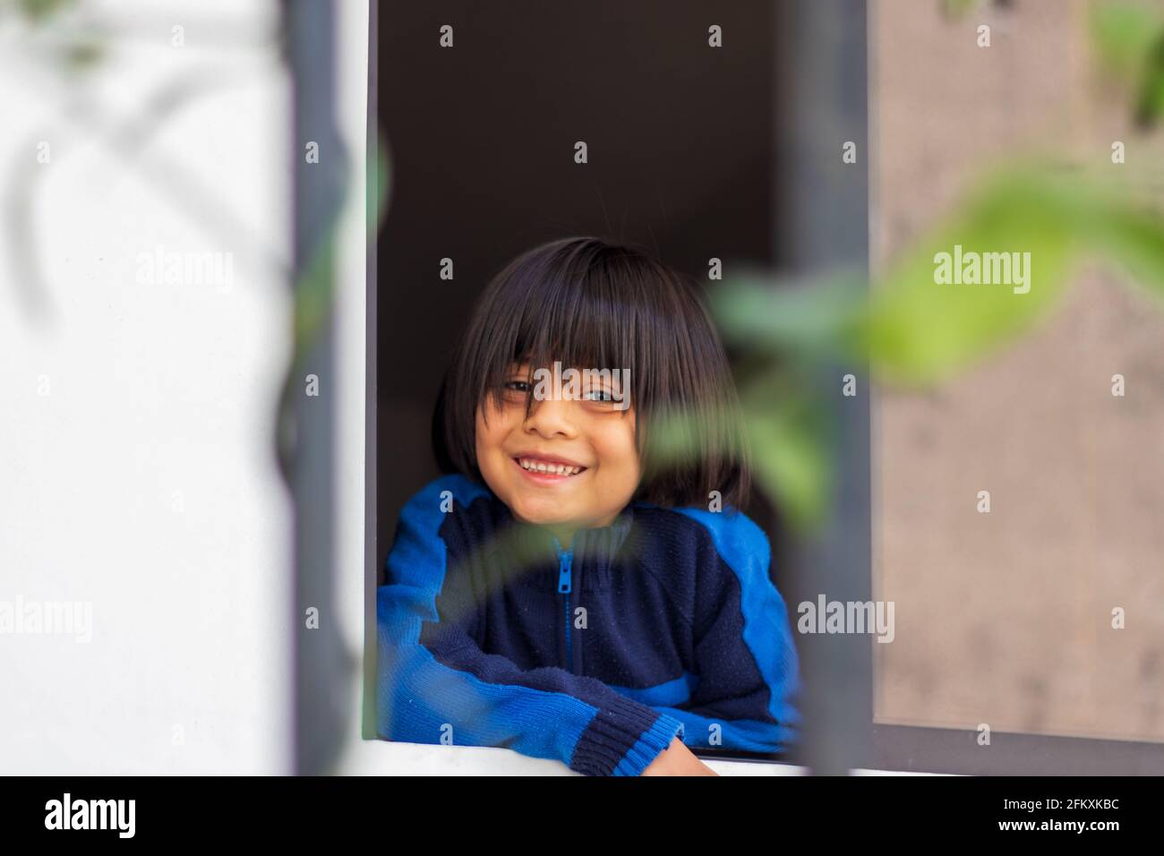 Niño chico hispano sonriendo desde una ventana, enfoque selectivo Foto de stock