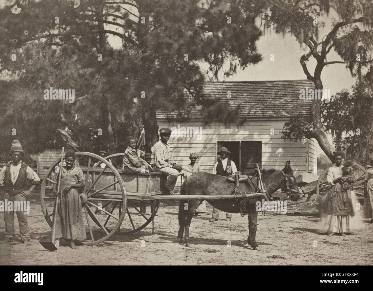 Esclavos negros 1862 Isla Edisto, S.C. (plantación de James Hopkinson) - La foto muestra un grupo de esclavos afroamericanos posados alrededor de un carro tirado por caballos, con un edificio en el fondo, en la plantación Cassina Point de James Hopkinson en la Isla Edisto, Carolina del Sur Foto de stock